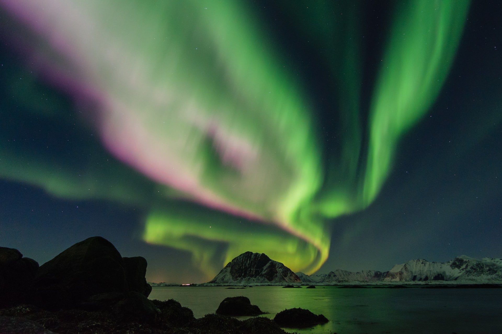 Northern lights over a lake and snow covered mountains